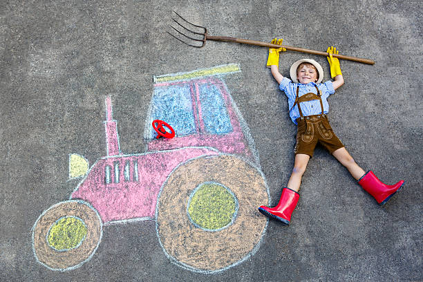 Adorable cute Asian toddler boy riding and play on an old tractor car parking in outdoor field happily. Young baby outdoor experience learning activity concept.