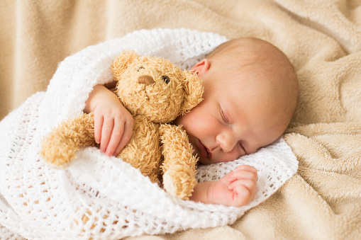 Infant sleeping together with teddy bear
