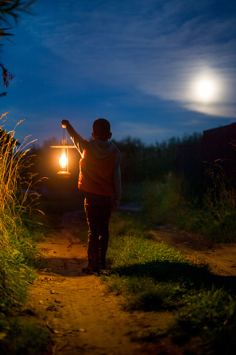 child with a lantern in his hand outdoors at night