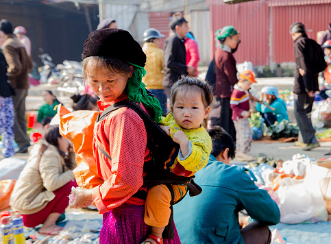 Ha Giang, Vietnam - Feb 14, 2016: Hmong little girl on her mother back in a local market in Dong Van district
