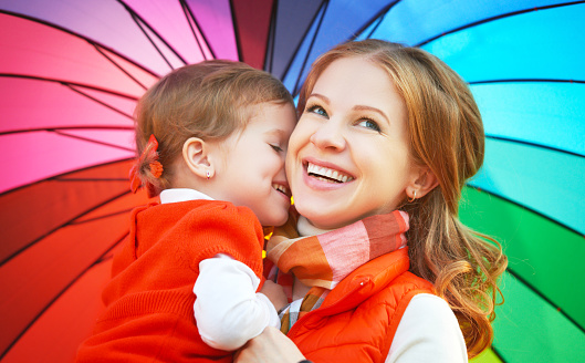 Happy family mum and child daughter with rainbow colored umbrella under rain on nature
