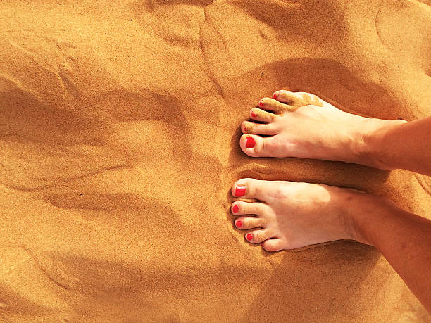 Close-up of a couple of feet in a resting position on the beach. Battered with sand. With textured background beach sand