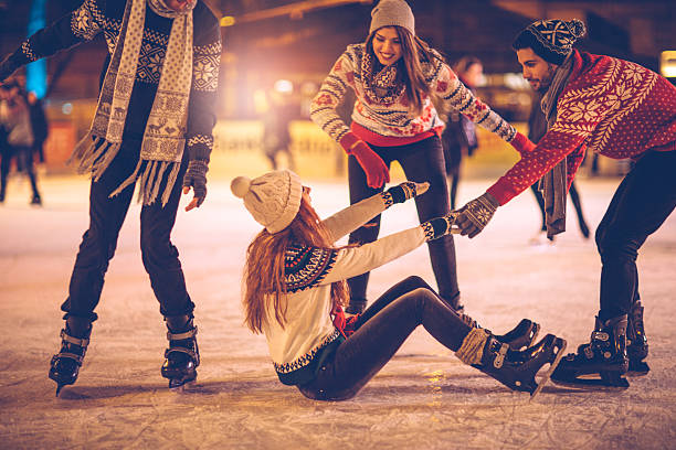 Let us help you Friends having so much fun while ice skating.  Wearing warm clothing. City is decorated with christmas lights. ice rink stock pictures, royalty-free photos & images