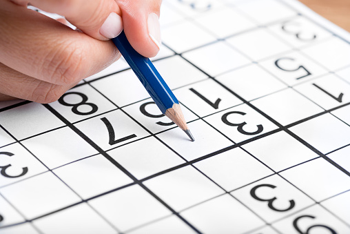 Woman hand holding a pencil and solving sudoku, popular puzzle game with numbers.