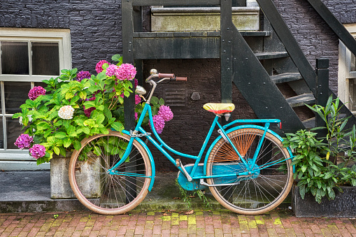 Pink bicycle with a basket of flowers against a brick wall