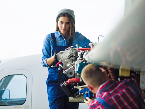 Female in uniform looking at her co-worker while repairing motor of air jet