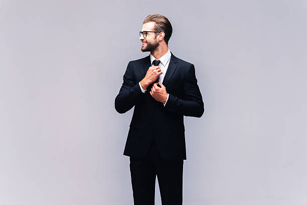 Confident businessman. Studio shot of handsome young man in full suit adjusting his necktie and smiling man adjusting tie stock pictures, royalty-free photos & images