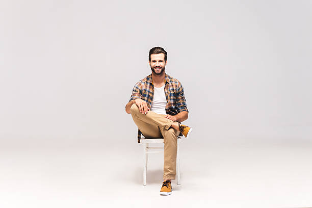 Casually handsome. Studio shot of handsome young man sitting on the chair and looking at camera with smile chair stock pictures, royalty-free photos & images