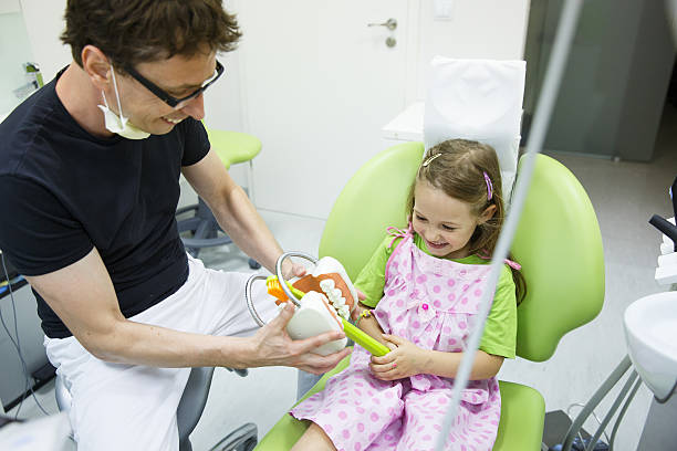 istock Girl in dentists chair tooth-brushing a model 589571380