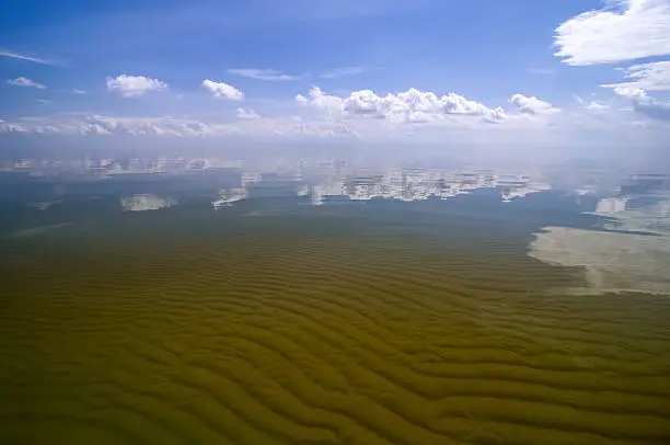 Sand waves are seen through transparent water surface of Curonian bay. Clouds are reflected in its smooth surface. Russia, Curonian spit