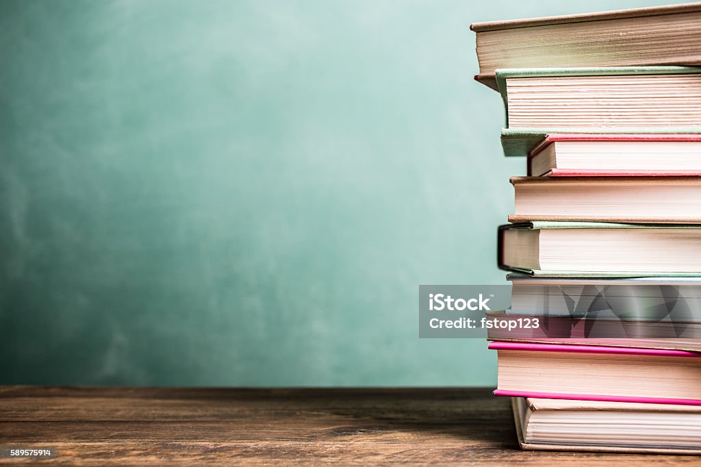 Libros de texto apilados en el escritorio de la escuela con fondo de pizarra. - Foto de stock de Libro libre de derechos