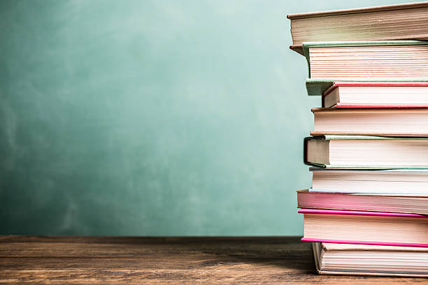 textbooks stacked on school desk with chalkboard background. - 書 圖片 個照片及圖片檔