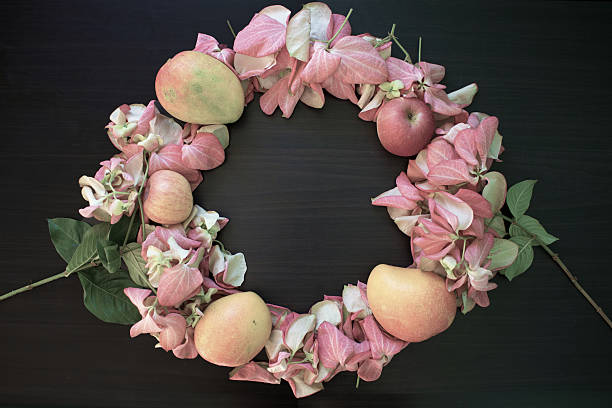 Wreath of pink tropical flowers and fruits Composition pink flowers and fruits forms natural frame on wooden table, round tropical flowers, wreath frame with pink flower mussaenda, apple and mango pink mussaenda flower stock pictures, royalty-free photos & images
