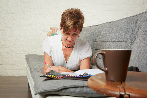 istock Senior woman on couch, drawing in coloring book 589579968