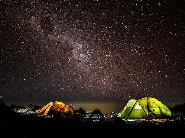 Night picture of camping tents with the milkyway and a city in the background shot at Kilimanjaro (Tanzania). Awesome for mountaineering publicty or adventure websites.