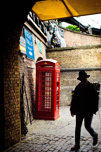 London,UK - March 6, 2016: Backlit man walking into Stables market in Camden, North London. In the baclground is a red GPO telephone box.