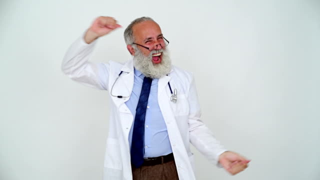 Adult cheerful senior doctor smiling and happy dancing on a gray background