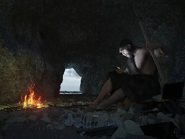 Photo of primitive man siting in the cave with smartphone concept illustration