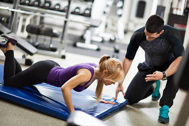 istock Fitness instructor motivating young woman doing push-ups at  gym. 589946732