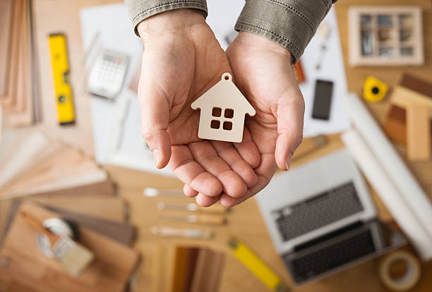 Housing concept Real estate agent holding a small house, desktop with tools, wood swatches and computer on background, top view rebuilding stock pictures, royalty-free photos & images