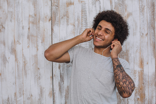 enjoy the sound. man, with curly hair wearing headphones, closed his eyes and smiling against retro wooden wall