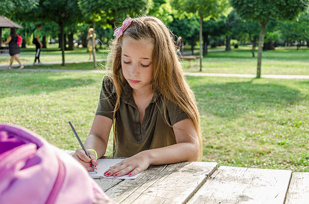 小さな女の子は木のテーブルの上に公園で描きます - schoolgirl little girls crayon human face ストックフォトと画像