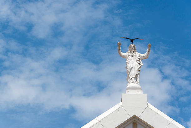 Statue of Jesus with a big black bird on his head on top of the Church of Saint Francis in  Panama City, located in the old town or casco viejo against a blue sky.