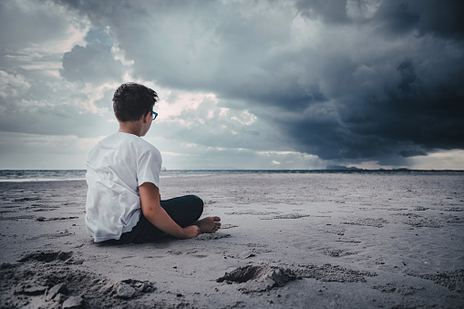 Boy sitting on the beach and looking forward. Stock Photo.