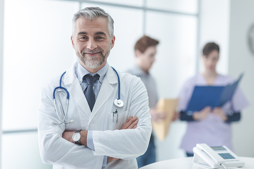 Confident doctor at the reception desk, he is posing with arms crossed and smiling at camera