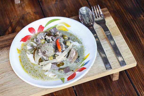 Green curry chicken with rice noodles on wooden table.