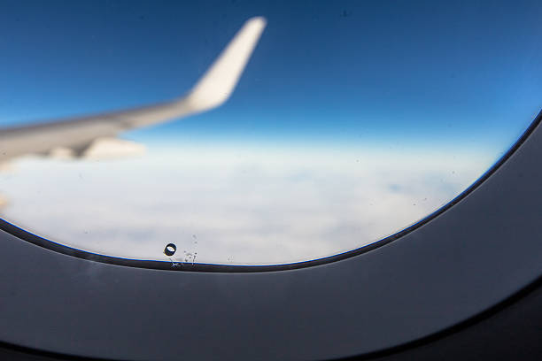 Airplane window breather hole bleed hole with wing blue sky stock photo