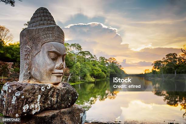 Stone Face Asura And Sunset Over Moat Angkor Thom Cambodia Stock Photo - Download Image Now
