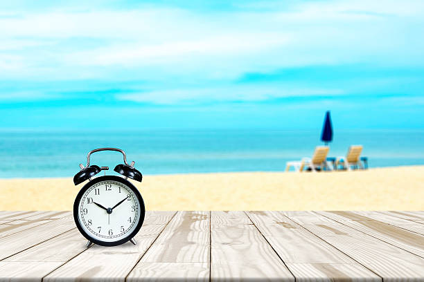 istock Alarm clock on wood table and sea beach blurred background 589974736