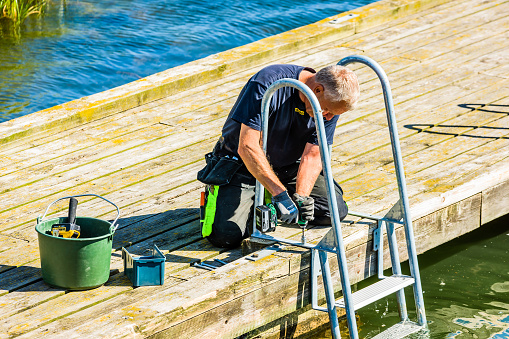 Kalmar, Sweden - August 10, 2016: Worker mounting a metal swim ladder on a public wooden pier.