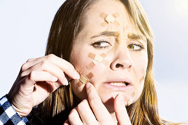 istock Upset woman adding sticking plaster to many on her face 590042542