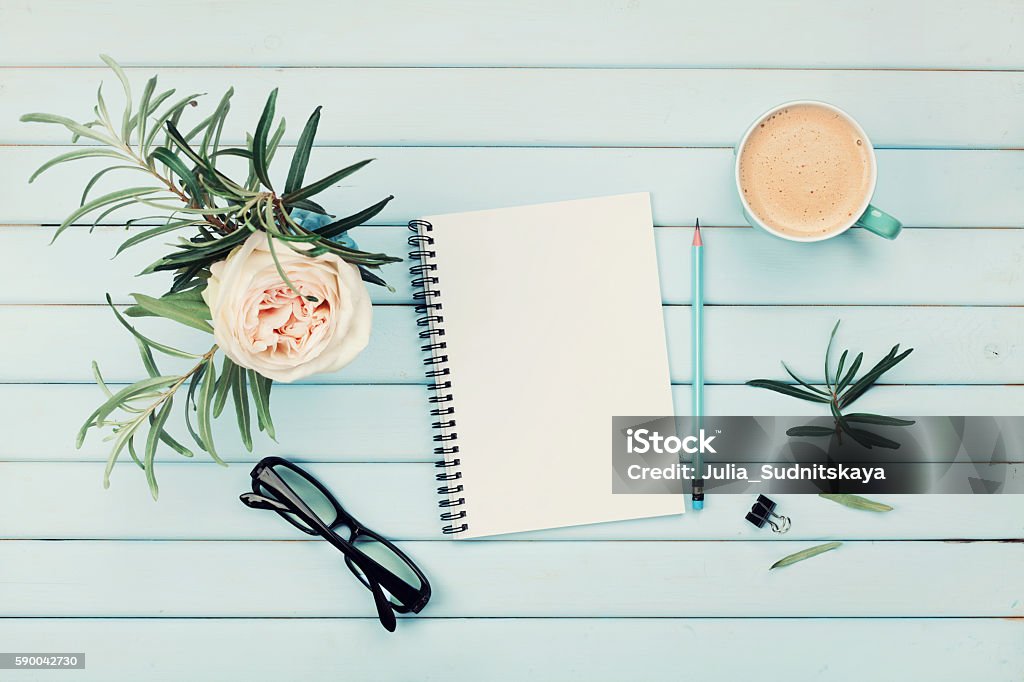 Planning and design concept. Cozy breakfast. Flat lay styling. Morning coffee cup, clean notebook, pencil, eyeglasses and vintage rose flower in vase on blue rustic table top view. Planning and design concept. Cozy breakfast. Flat lay styling. Desk Stock Photo