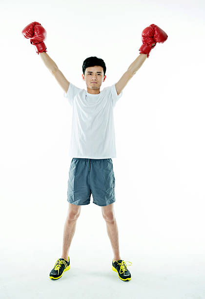 Young asian man cheering in boxing gloves against white background.