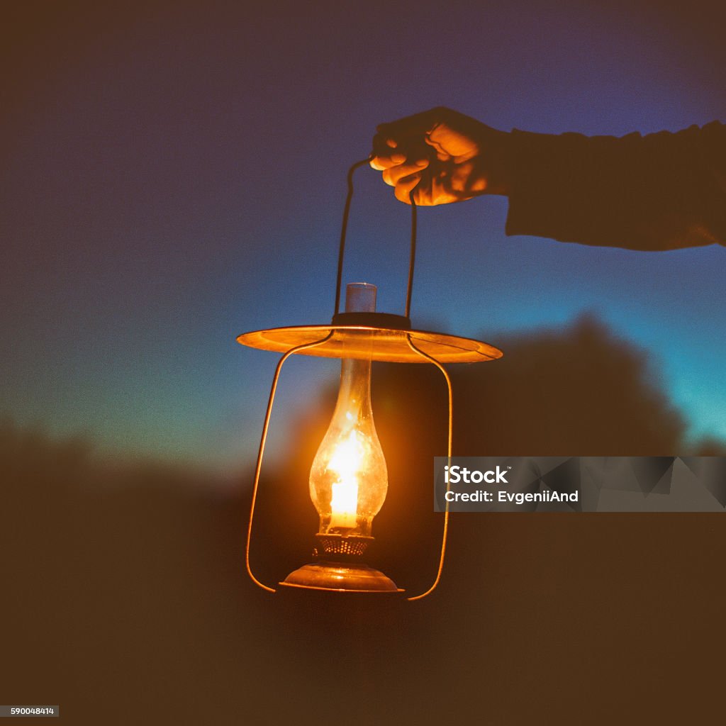 hand holds a large lamp outdoors in the dark old lamp with a candle illuminates the way on a dark night. dim lightб Holding Stock Photo