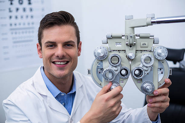 Smiling optometrist adjusting phoropter Smiling optometrist adjusting phoropter in ophthalmology clinic Messbrille stock pictures, royalty-free photos & images