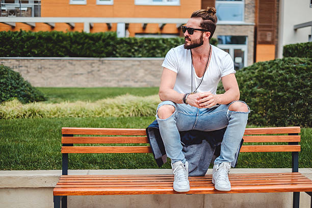 Hipster with man bun sitting on the park bench stock photo