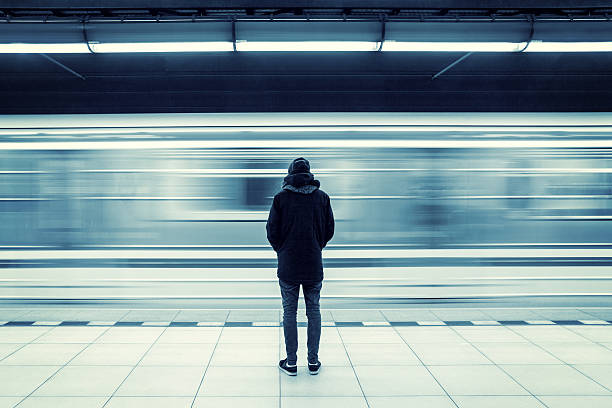 Man at subway station Lonely young man shot from behind at subway station with blurry moving train in background subway platform stock pictures, royalty-free photos & images