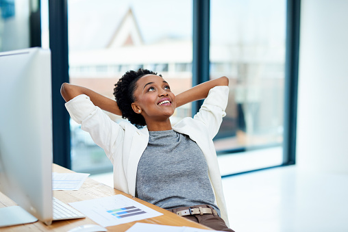 Cropped shot of a young woman sitting with her hands behind her head in the office