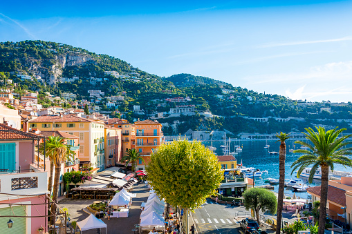 Villefranche-sur-Mer, France - August 12, 2016: The town and harbour of Villefranche-sur-Mer on the Cote d'Azur, South of France. Various people are looking at a market, walking along the harbour and street. Shops signs and boat livery.