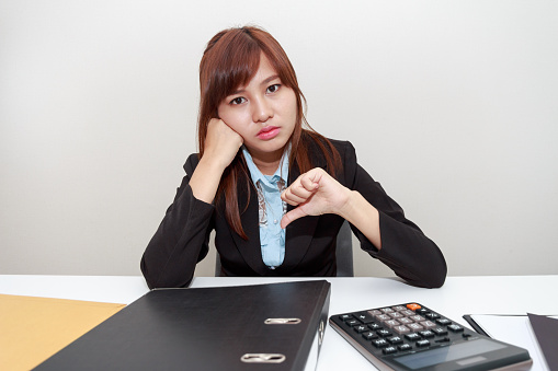 Unhappy business woman with thumb down in office - calculator, file and document on desk