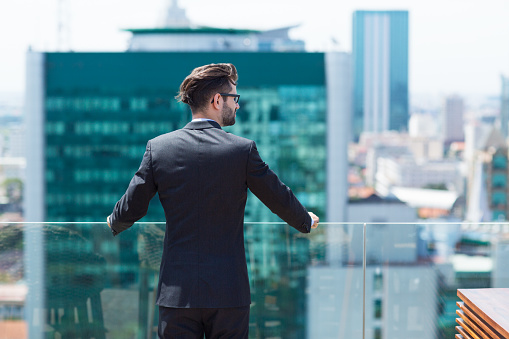 Portrait of young businessman standing on balcony and looking at city view