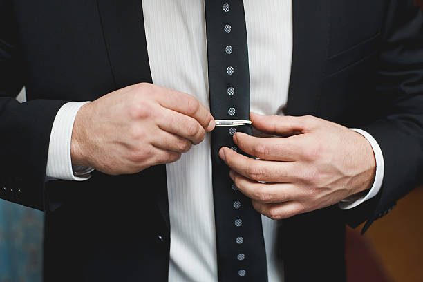 istock Man in black suit putting on tie clip 590060306