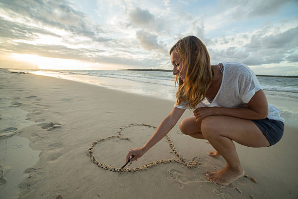 istock Caucasian female draws a heart shape on sand 590066828