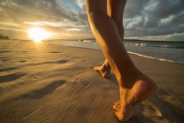 Barefoot on beach walking towards sunlight Young woman walking on a beach making foot print on the sand. Sun setting on the sea. Barefoot stock pictures, royalty-free photos & images