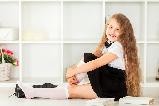 smiling little schoolgirl in school uniform sitting near bookshelf