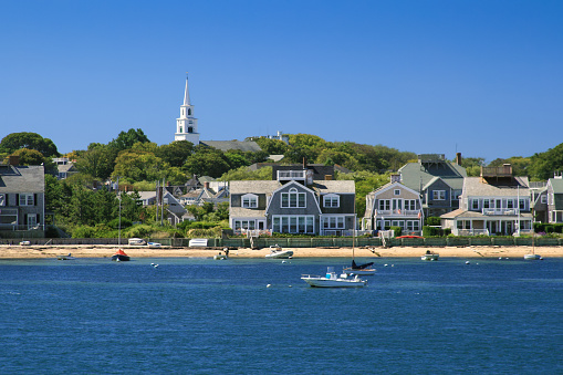 Harbor View with Boats and Waterfront Houses, Nantucket Island, Massachusetts, USA. Moored sailboats and motorboats, American flags, green trees, sandy shore and vivid blue clear sky with some clouds are in the image. Polarizing filter